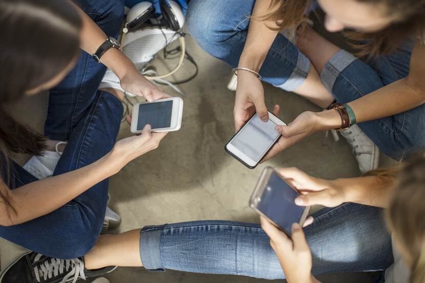 Drie jongeren zittend op de grond met mobiel in hun hand